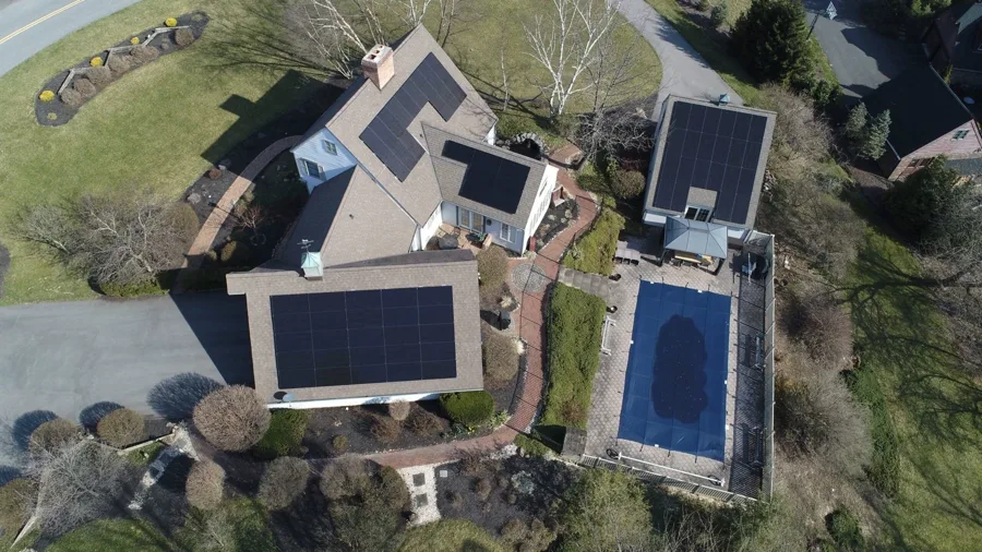Aerial view of a home with solar arrays on the main roof and pool house.